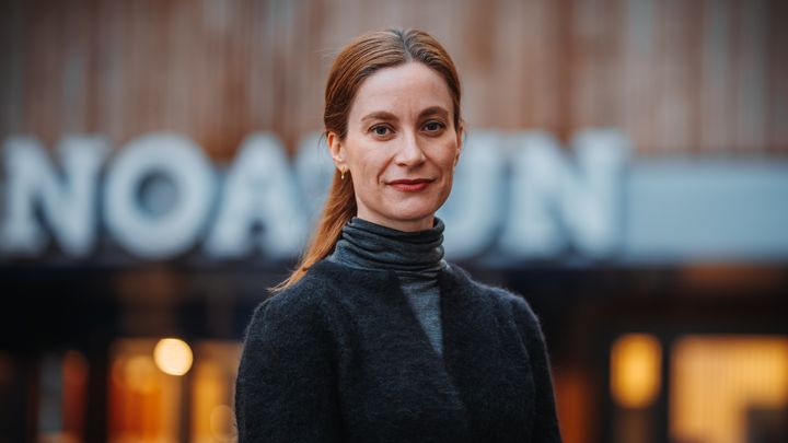 Portrett av kvinne ute foran bygg med store bokstaver.