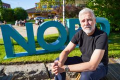 Bilde av mannlig voksen forsker sitter ute i en park foran logoen til Nord universitet.