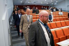 Flere voksne menn i dress som går ned en trapp i en forelesningssal.