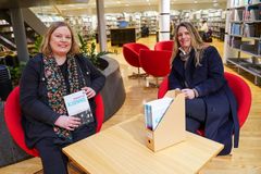 To kvinner som sitter i hver sin røde stol i et bibliotek
