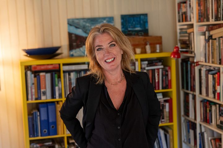 Bilde av voksen kvinne i svart skjorte som står foran bokhyller inne i en stue.