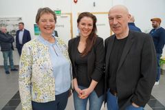 To kvinner og en mann som smiler og ser i kamera, med andre mennesker i bakgrunn.