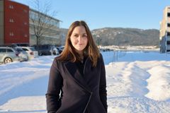 Nærbilde av kvinne som står ute i en gate. Det er vinter, mye snø og blå himmel.