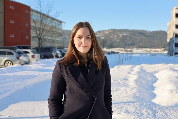 Nærbilde av kvinne som står ute i en gate. Det er vinter, mye snø og blå himmel.