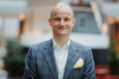 Voksen mann i lys blå dressjakke og hvit skjorte. Han ser rett i kamera, han smiler og han står inne.