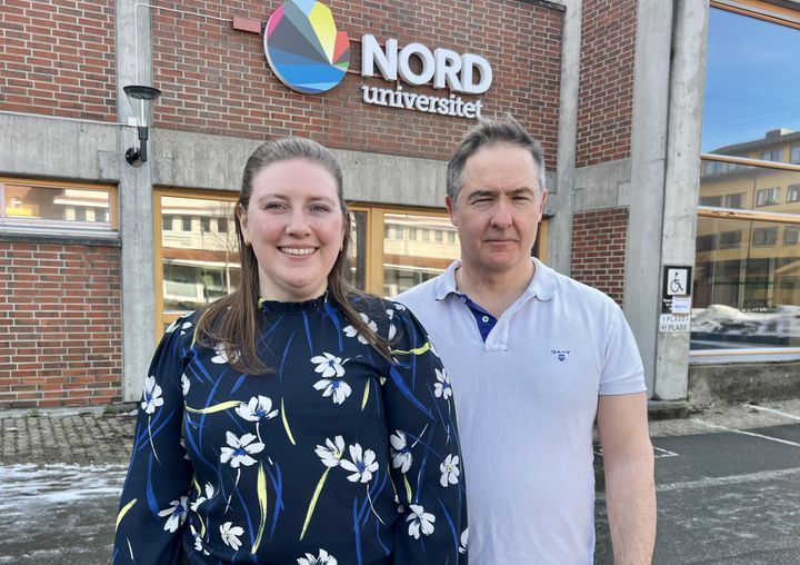 To voksne personer - en kvinne og en mann - foran en bygning. De står ute og det er pent vær.