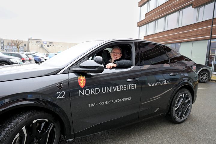 Voksen mann bak rattet i en sort bil. Han har armen hvilende i det åpne vinduet. Det er overskyet.