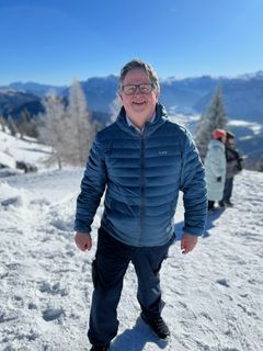 Voksen mann i blå boblejakke som står ute. Det er vinter, snø og blå himmel.