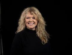 Portrett av voksen kvinne. Bakgrunnen er helt sort. Bildet er tatt i et fotostudio.