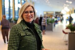 Portrett av voksen kvinne med grønn jakke. Bildet er tatt inne i en stor og lys foaje, og det er mennesker i bakgrunnen.