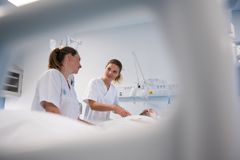 To unge kvinnelige sykepleiestudenter ved siden av en seng.