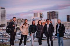 Seks unge studenter som står ute i en by. Bak ser vi flere høye bygninger.