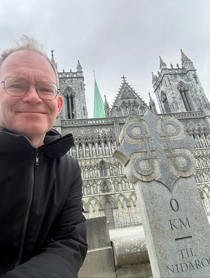 Smilende mann ved milestienen foran Nidarosdomens vestfront.