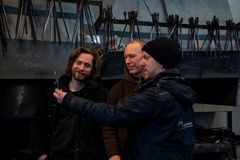 Tre menn står i en smie og ser på et lite dekorelement i smijern.