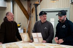 Tre menn står i et verksted og ser på noen treplater.