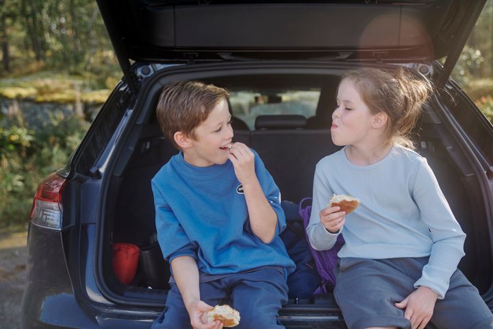 Jente og gutt har rastepause i bakluken på bil