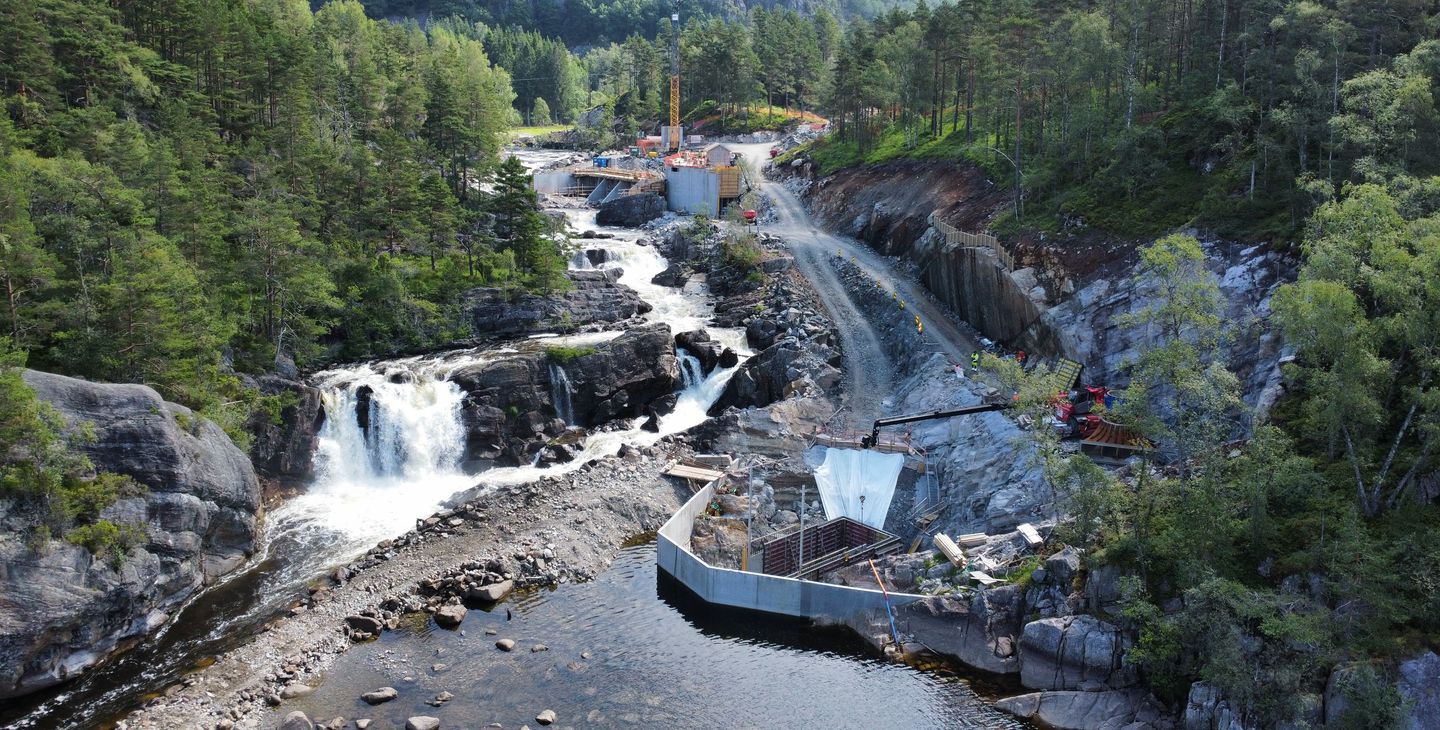 Anleggsområde, anleggsmaskiner, foss, vann, skog. Foto.