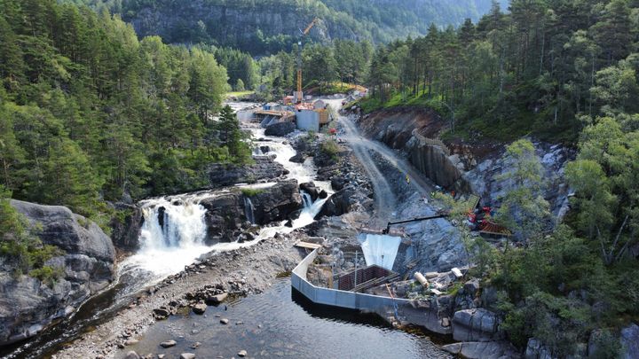 Anleggsområde, anleggsmaskiner, foss, vann, skog. Foto.