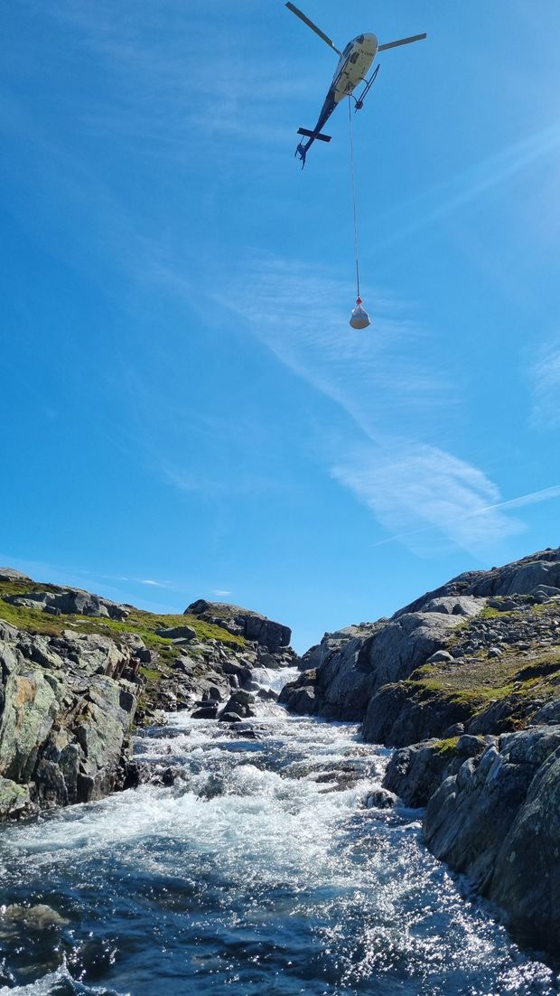 Helikopter, himmel, fjellterreng, bekk grus. Foto.