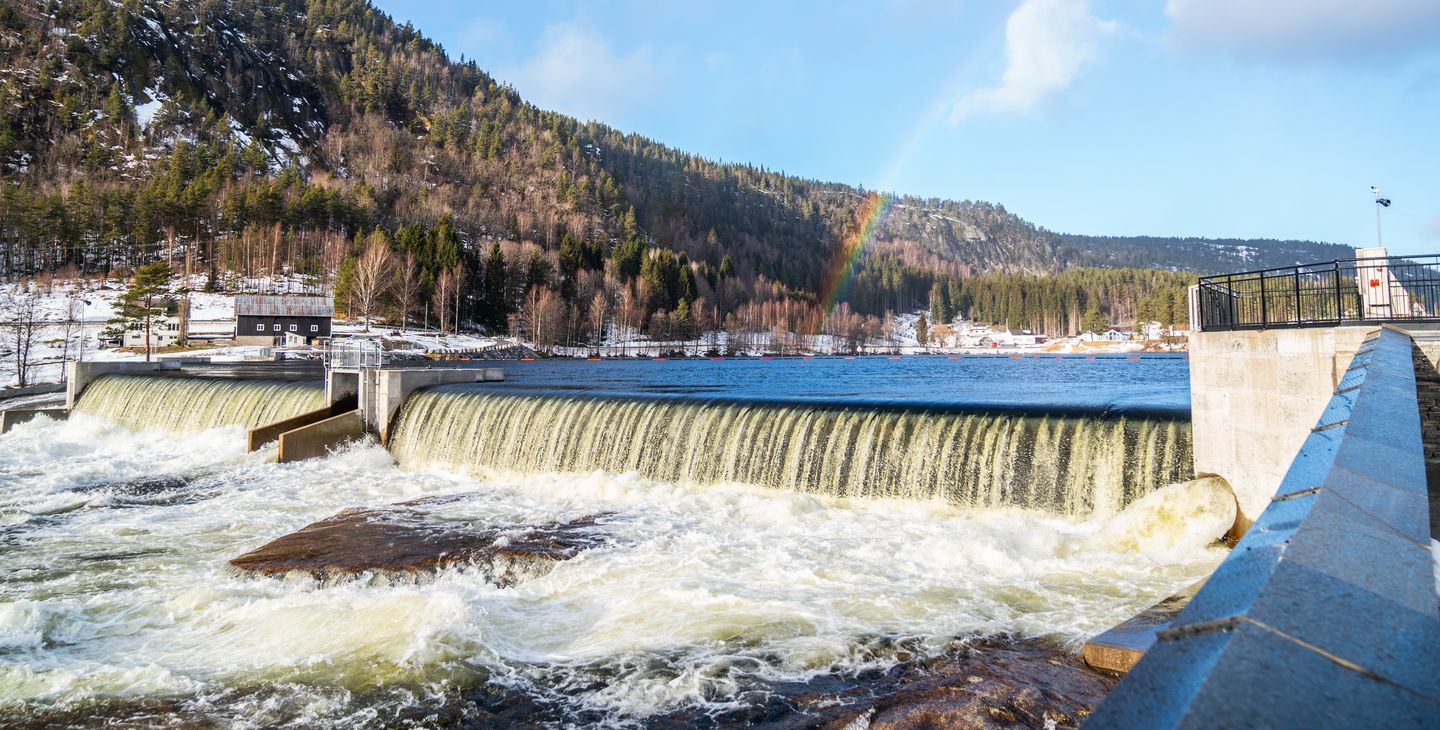 Elv, dam, gårdsbygning, fjell, skog, himmel, skyer, regnbue. Foto.