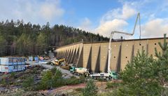 Dam, anleggsmaskiner, anleggsbrakker, skog, himmel. Foto.