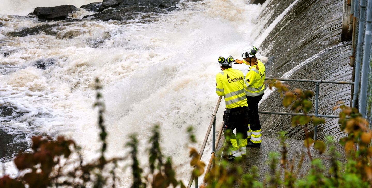 Kraftverksdam, vann, to personer i arbeidstøy. Foto.