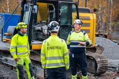 Tre menn, vernetøy, gravemaskin, anleggsområde. Foto.