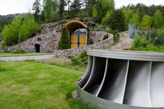 Inngang til kraftverk i fjell, maskindel, plen, skog, himmel. Foto.