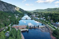 Kraftverk, elv, luker, bygdesentrum, skog, fjell, himmel. Foto.