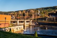 Kraftverk, elv, luker, bygdesentrum, skog, himmel. Foto.