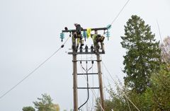 To menn, strømmast, trær, himmel. Foto.