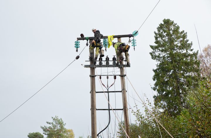 To menn, strømmast, trær, himmel. Foto.