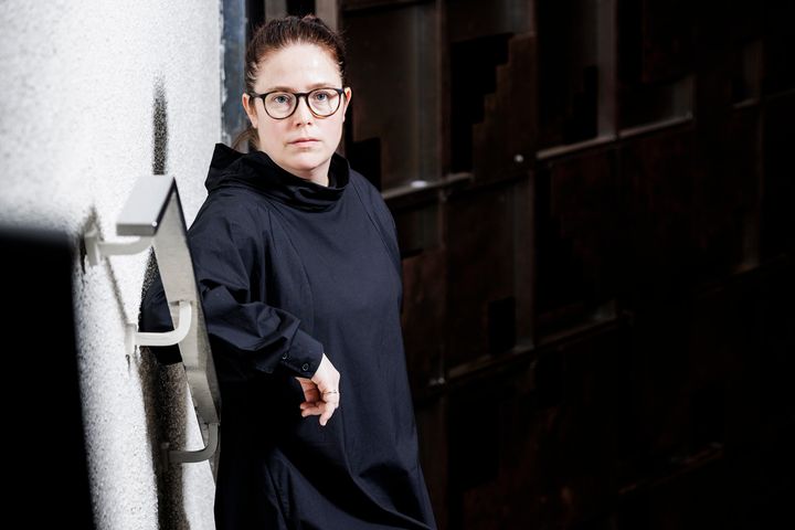 Kjersti Barsok står lent mot en vegg i en trapp med et alvorlig blikk og mørk kjole.