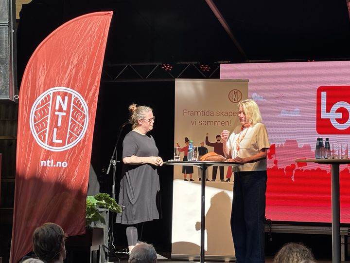 Scene med NTL-beachflagg, NTL-rollup og LO-grafikk på skjerm. NTLs forbundsleder prater med Marie Simonsen.