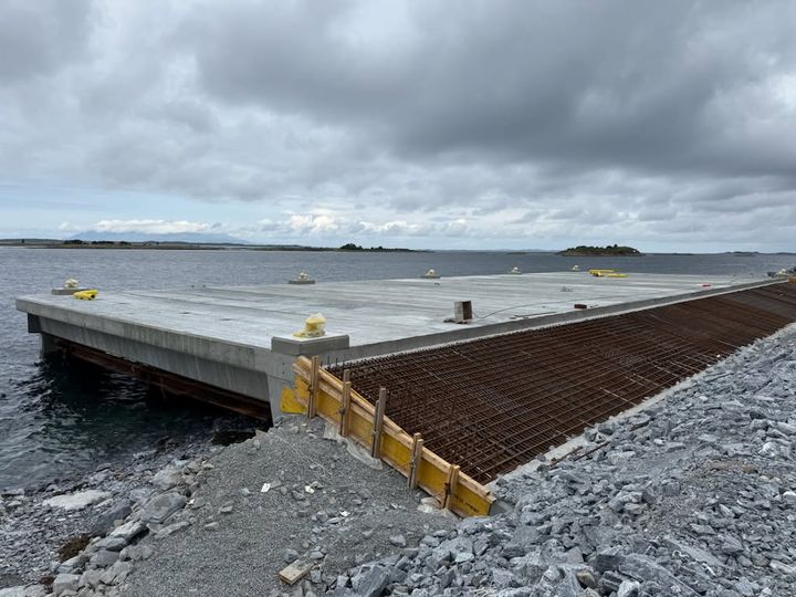 Bildet viser Gårdsøya tømmerkai under bygging i Brønnøy kommune. En betongkai med grå sjø i bakgrunnen.