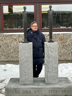 To bronseskulpturer står på hver sin granittsokkel, som igjen er montert sammen i en betongsokkel med tittelen 'Finne vår vei' støpt inn i betongen. Kunstner Tove Hirth står bak skulpturen.