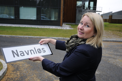 Kvinnelig ansatt i Kartverket med gatenavn-skilt med påskriften "Navnløs". Foto: Sveinung Engeland/ Kartverket