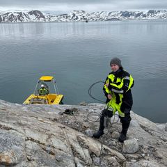 Hydrograf Ingeborg Andrea Sylte-Raanes holder vaieren til en vannstandmåler. en Mobbåt ligger til ankers i bakgrunnen.