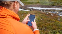 Person i oransje jakke sjekker turkart på en mobiltelefon ute i naturen.