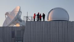 Fire personer står på en plattform ved siden av satellittantenner under første steg av installasjonen av SLR ved jordobservatoriet i Ny-Ålesund.