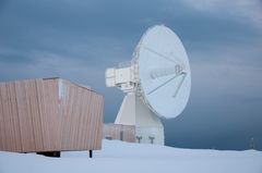 En stor, hvit VLBI-antenne ved det geodetiske jordobservatoriet i Ny-Ålesund, Svalbard, omgitt av snø.