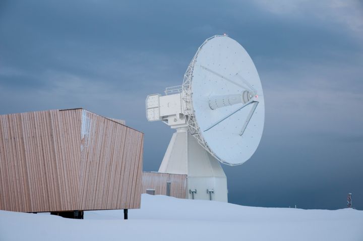 En stor, hvit VLBI-antenne ved det geodetiske jordobservatoriet i Ny-Ålesund, Svalbard, omgitt av snø.