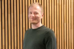 Person i grønn genser foran en vegg med trepaneler.