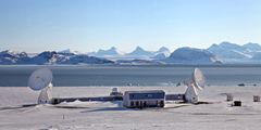 Kartverkets jordobservatorium i Ny-Ålesund i et snødekt landskap med hav og fjell i bakgrunnen.