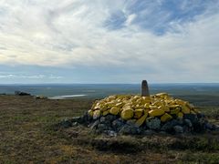 Riksrøys 325 markerer den norsk-finske grensen. Stabel av gule steiner med en grensemarkør på toppen, omgitt av åpne landskaper.