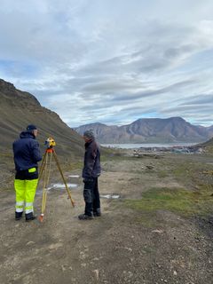 To personer arbeider med målerutstyr i et kupert landskap på Svalbard.