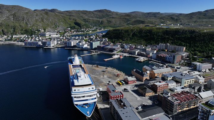 Luftfoto av Hammerfest havn med et cruiseskip til kai, omgitt av by og fjell.