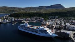 Utsikt over Hammerfest havn med et stort cruiseskip til kai, omgitt av by og landskap.