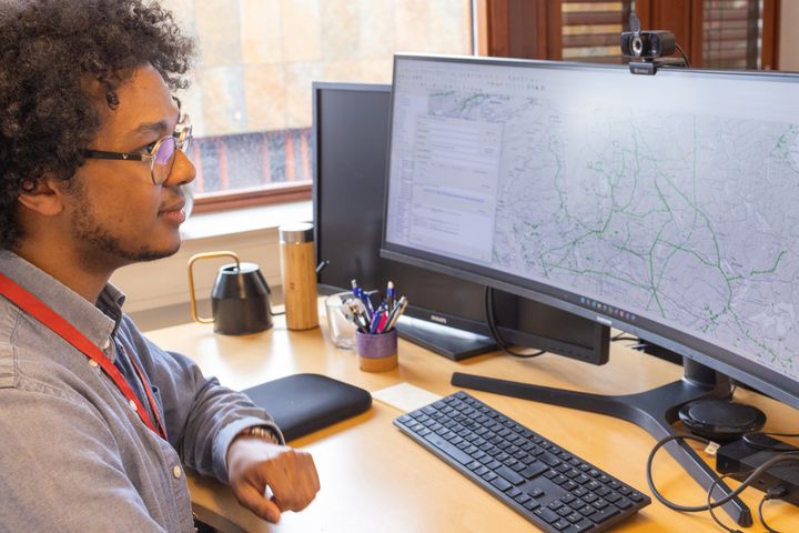Person som sitter ved et skrivebord og ser på geografiske data på en stor skjerm.