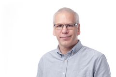 En mann i lyseblå skjorte og briller smiler.
